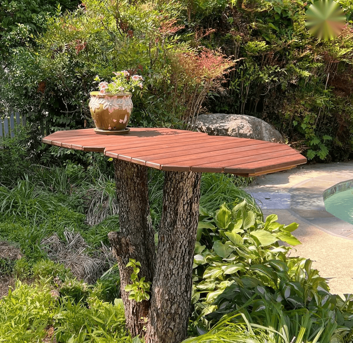 Shaped slatted wooden tabletop supported by a tree-trunk base in a garden