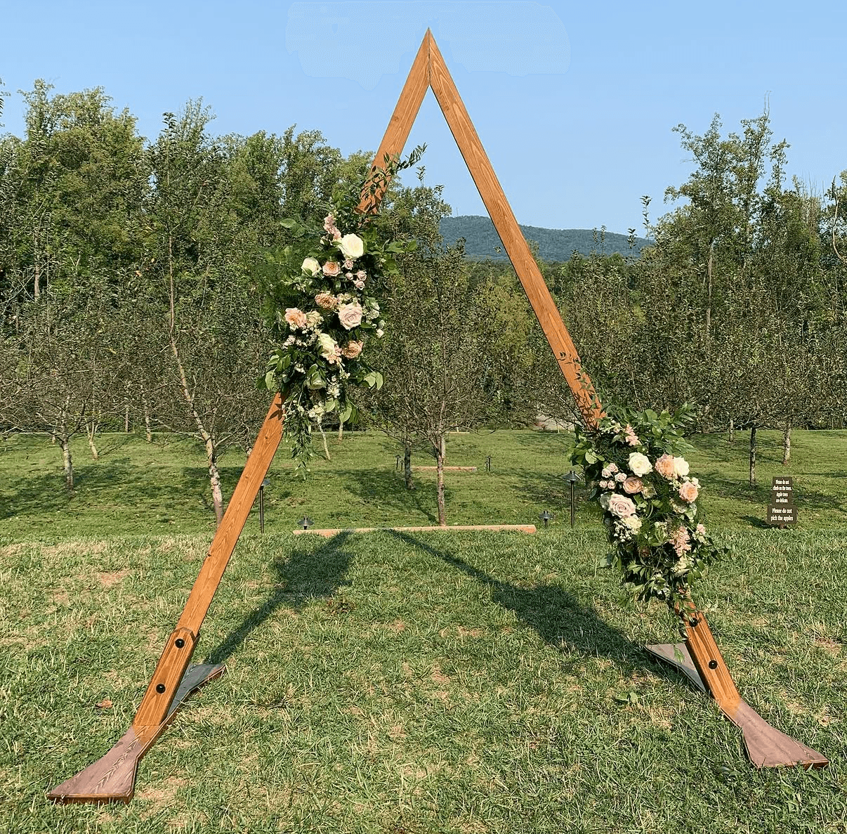 Triangular wooden wedding arch decorated with flowers on a lawn